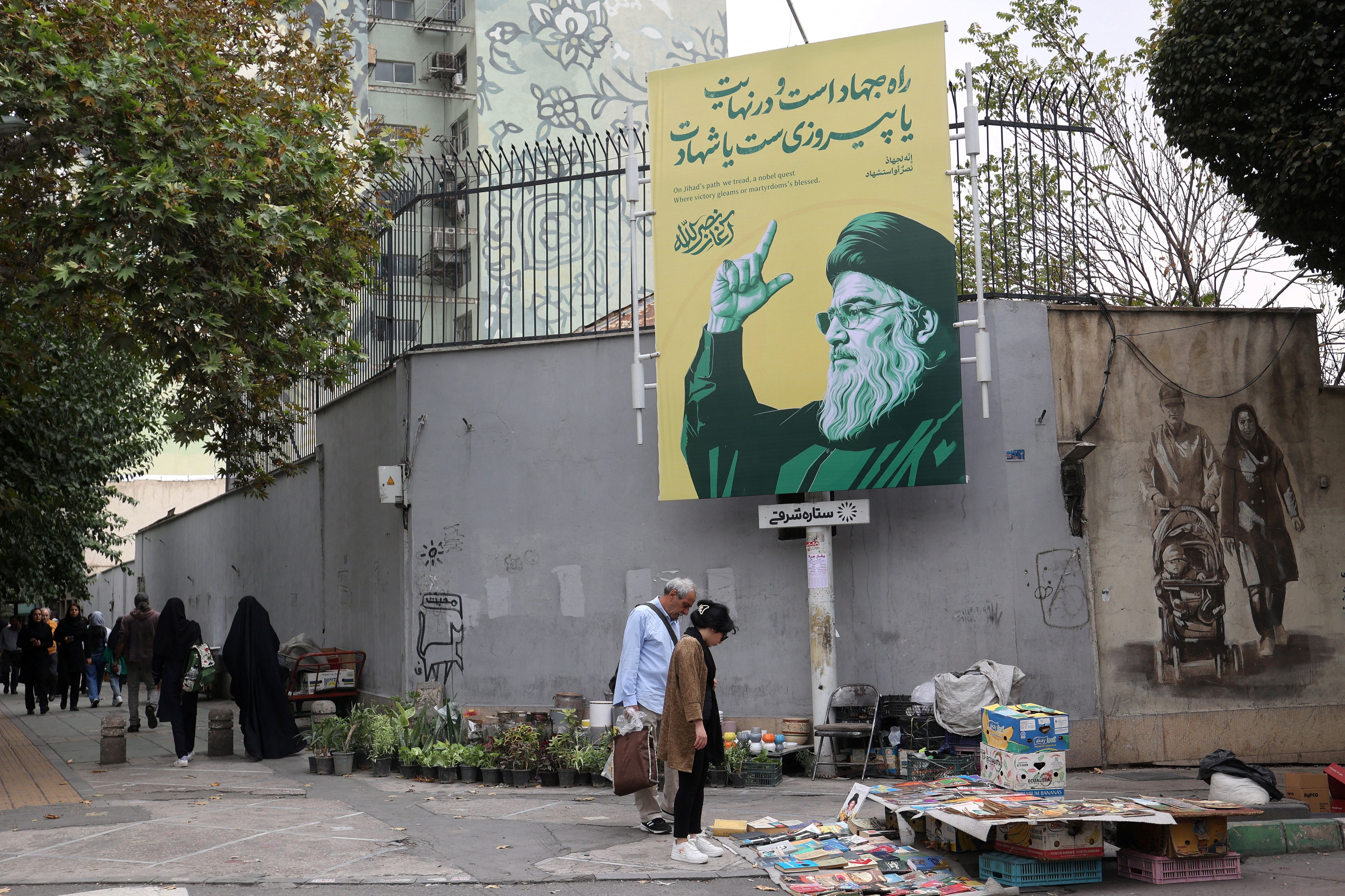 People stand next to a banner with a picture of the late Lebanon's Hezbollah leader Hassan Nasrallah, in a street in Tehran, Iran September 29, 2024. 