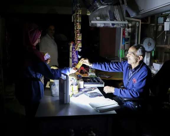People shop in a grocery store under a portable electric light during a power cut near Bhamdoun, Lebanon, October 9, 2021.