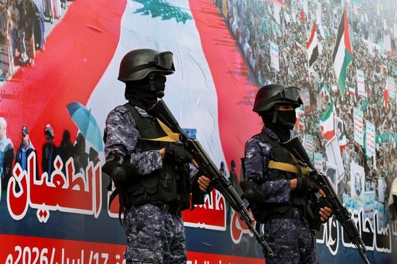 This photograph captures two armed soldiers standing in front of a large Lebanese flag during a public event. The scene appears to be part of a security operation or demonstration, with the soldiers positioned in front of a crowd.