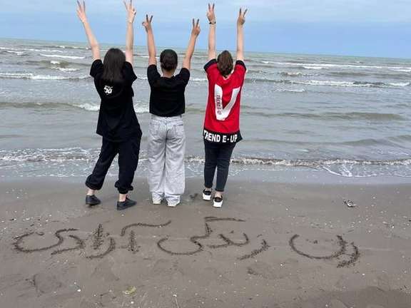 Young women with the slogan "Woman, Life, Freedom" written on the sand
