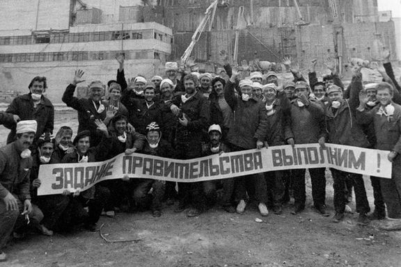 عکس کارگران پس از تلاش برای مهار پیامدهای فاجعه چرنوبیل، نوامبر ۱۹۸۶؛ بر بنری که در دست دارند، نوشته شده است: «ما هدف حکومت را محقق میکنیم.»