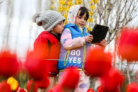Children look at a mobile device among spring tulips in a flower garden in Tabriz, northwestern Iran, May 24, 2026