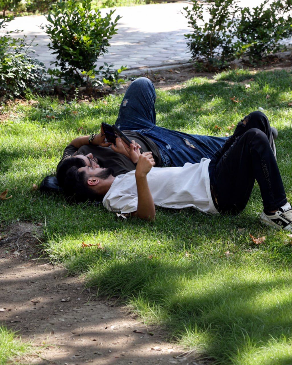 Young Iranians look at their mobile phone as they rest in a park in Tehran