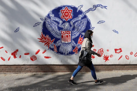 An Iranian woman wearing a face mask walks past a wall of the former U.S. embassy in Tehran, Iran, April 6, 2021.