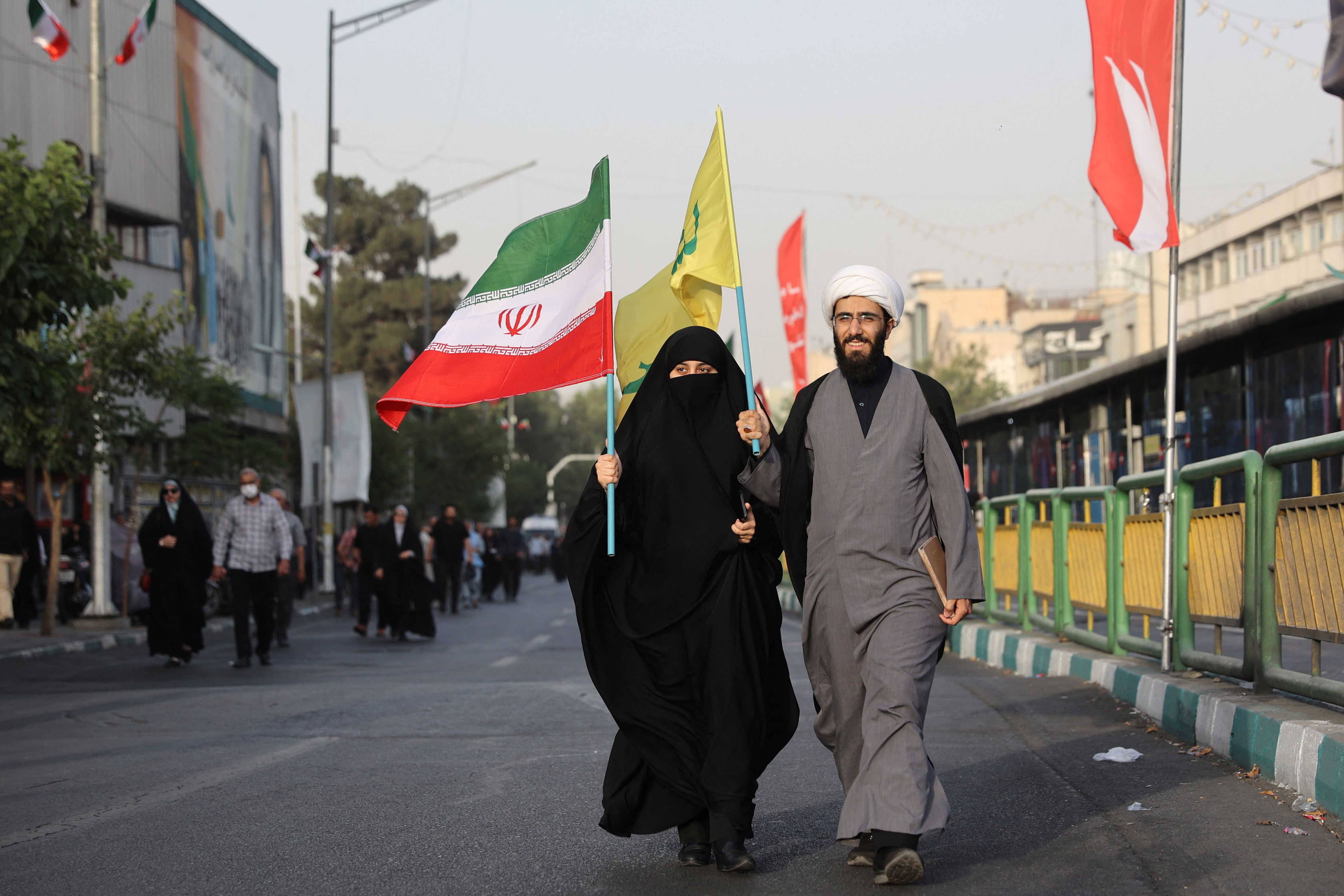 A cleric and his wife carry Iranian and Hezbollah flags as they attend a gathering to support Iran's Armed Forces after US President Donald Trump announced a ceasefire between Israel and Iran, in Tehran, Iran, June 24, 2025. 