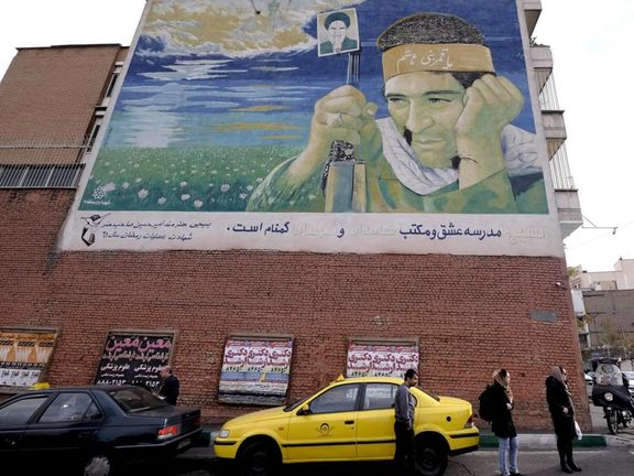 People standing under a worn-out mural depicting a soldier killed in the Iraq-Iran war, Tehran, Iran, Dec. 2015