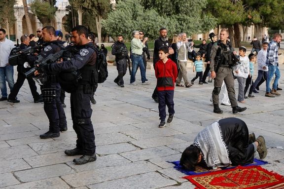 Members of the Israeli security forces stand near Palestinian people praying at the Al-Aqsa compound, also known to Jews as the Temple Mount, while tension arises during clashes in Jerusalem's Old City, April 9, 2023