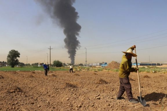 Farmers work in a field as smoke from an oil refinery rises in the background, in Tehran, Iran June 3, 2021.