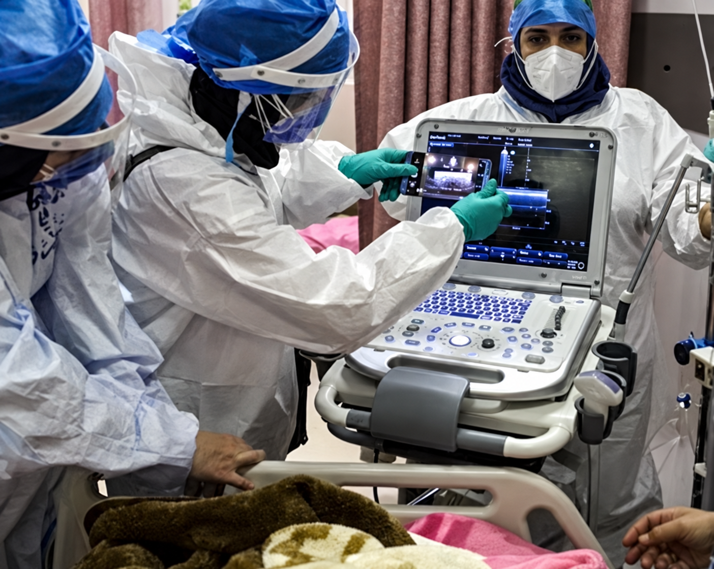 Healthcare workers wearing protective equipment operate an ultrasound machine at a hospital in Iran.