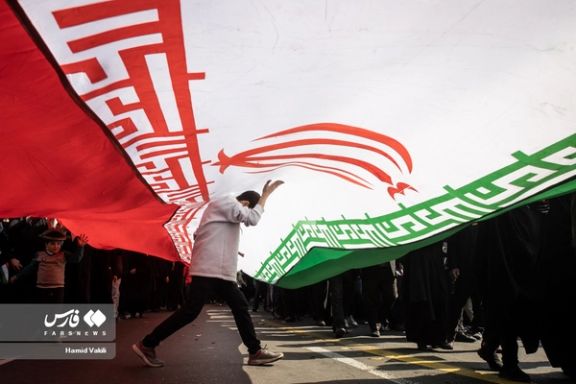 People walking under a large Islamic Republic flag during regime-sponsored demonstrations to mark the 45th anniversary of Islamic Republic establishment, Tehran, February 11, 2024