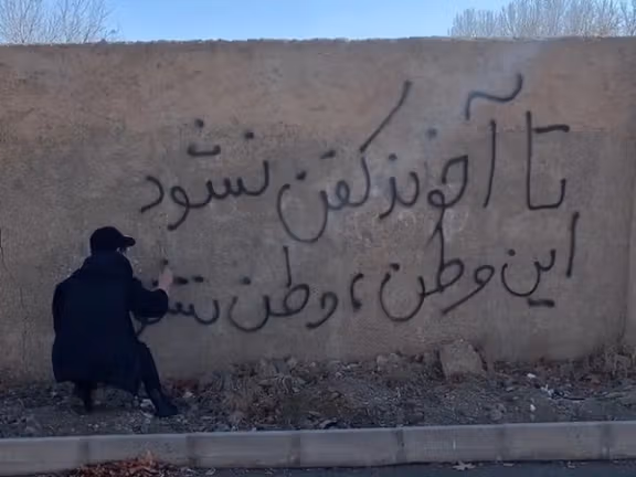 An Iranian protester spraying a slogan on the wall that reads: "Until the mullah is shrouded, this land will not be a homeland."