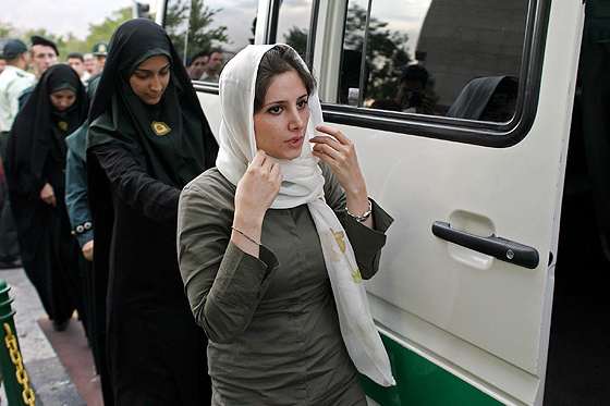 The woman in white scarf stopped by female hijab police in the street, who are taking her into a police van