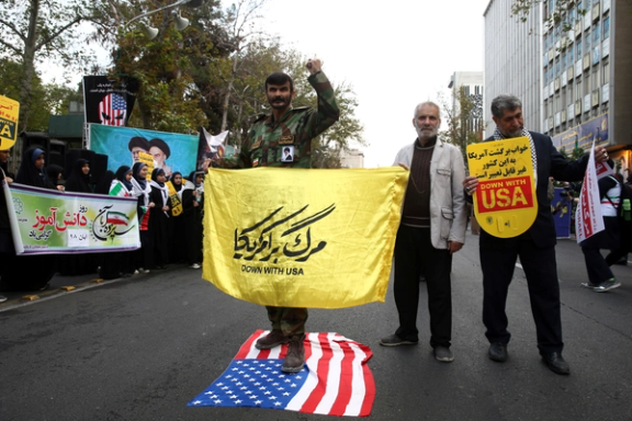 An Iranian man stands on a US flag, as they attend an anti US demonstration, marking the 40th anniversary of the U.S. embassy takeover, near the old US embassy in Tehran, Iran November 4, 2019.