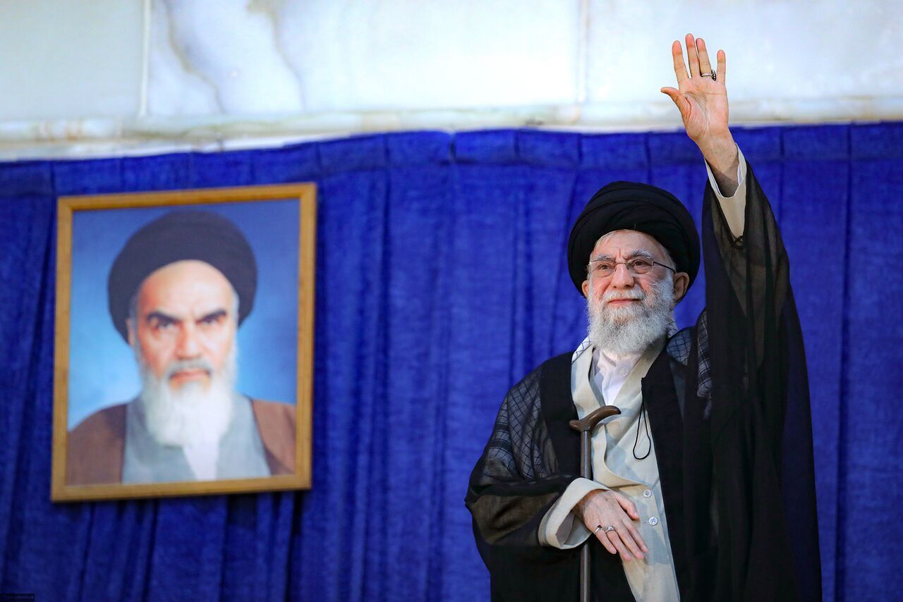 Iran's supreme leader Ali Khamenei waving to supporters, with a framed picture of his predecessor Ruhollah Khomeini behind him