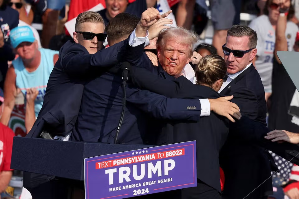 Republican presidential candidate and former US President Donald Trump gestures with a bloodied face while he is assisted by US Secret Service personnel after he was shot in the right ear during a campaign rally at the Butler Farm Show in Butler, Pennsylvania, US, July 13, 2024.