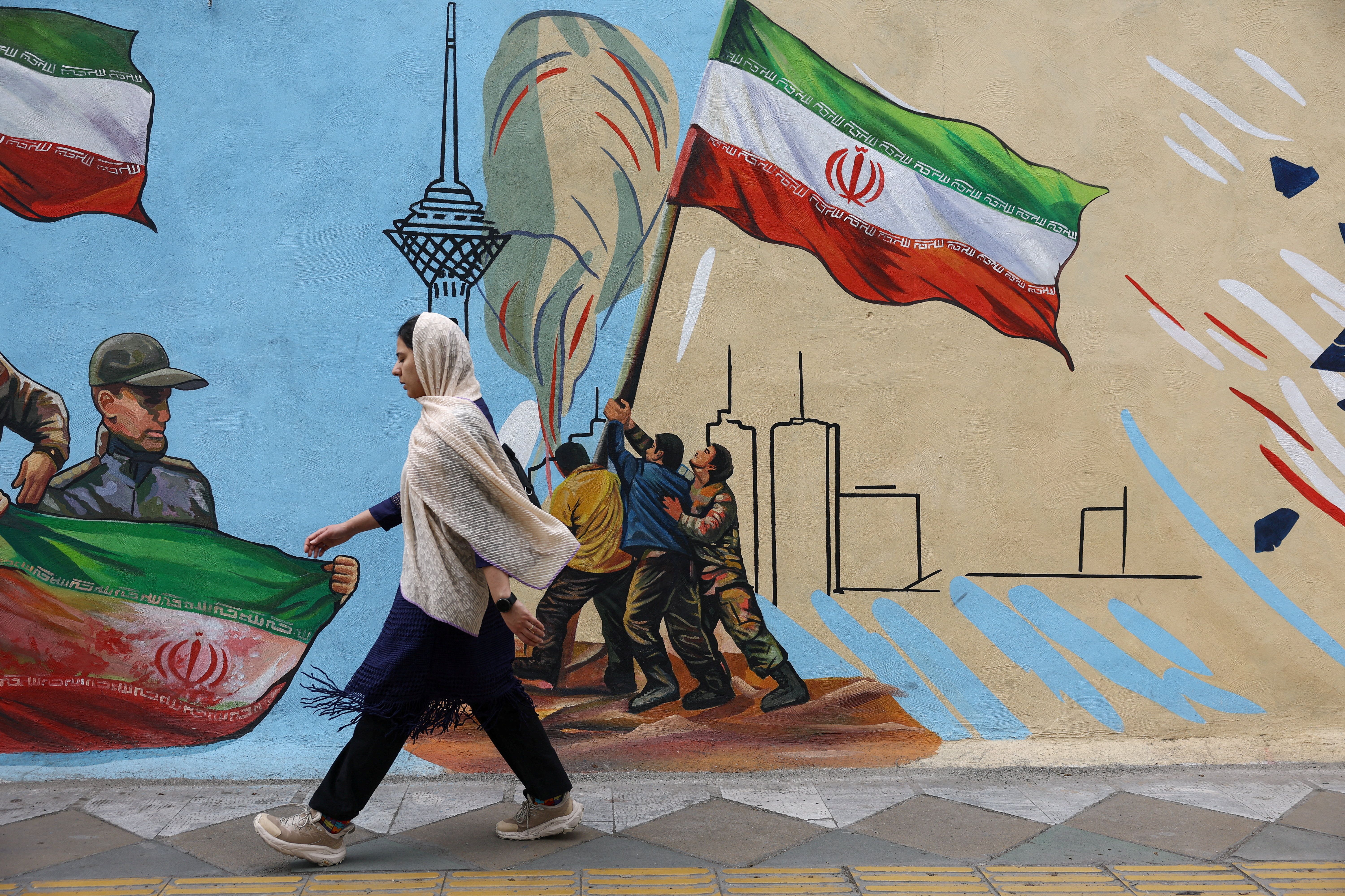 An Iranian woman walks next to a mural on a street in Tehran, Iran, May 5, 2026. 