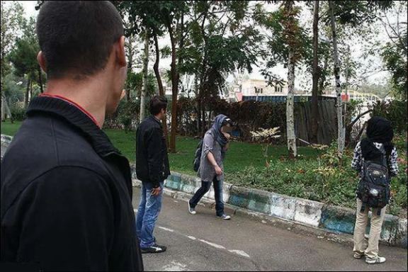 Two young women walk along a sidewalk while being closely watched and harassed by some men. (Undated)