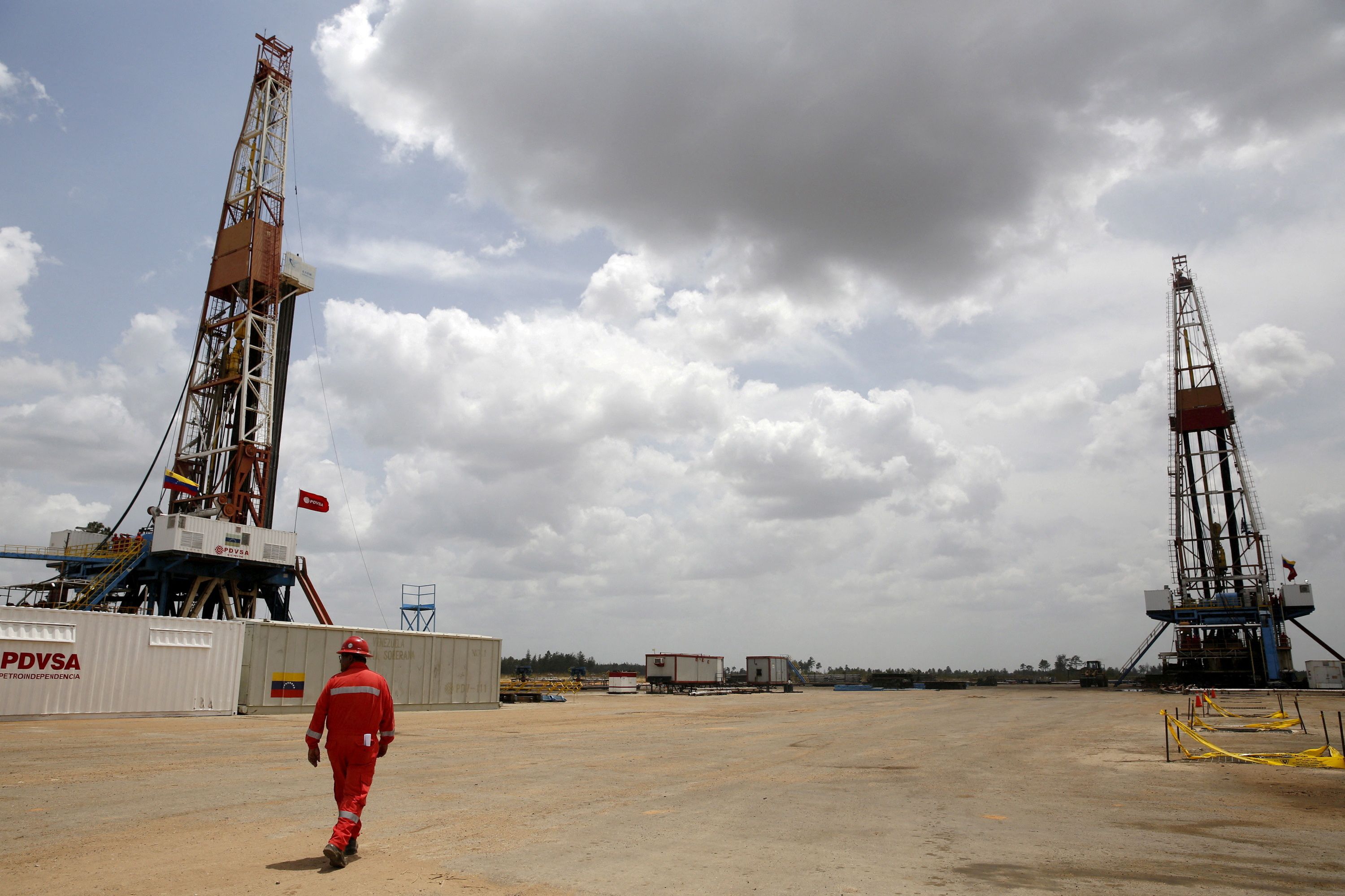 An oilfield worker walks next to drilling rigs at an oil well operated by Venezuela's state oil company PDVSA, in the oil-rich Orinoco belt, April 16, 2015.
