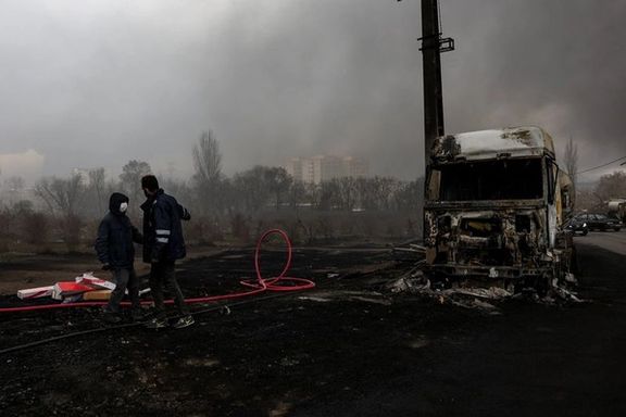 People stand near a destroyed vehicle as smoke rises after a reported strike on Tehran's Shahran fuel tanks, amid the US-Israeli war Iran, March 8, 2026.