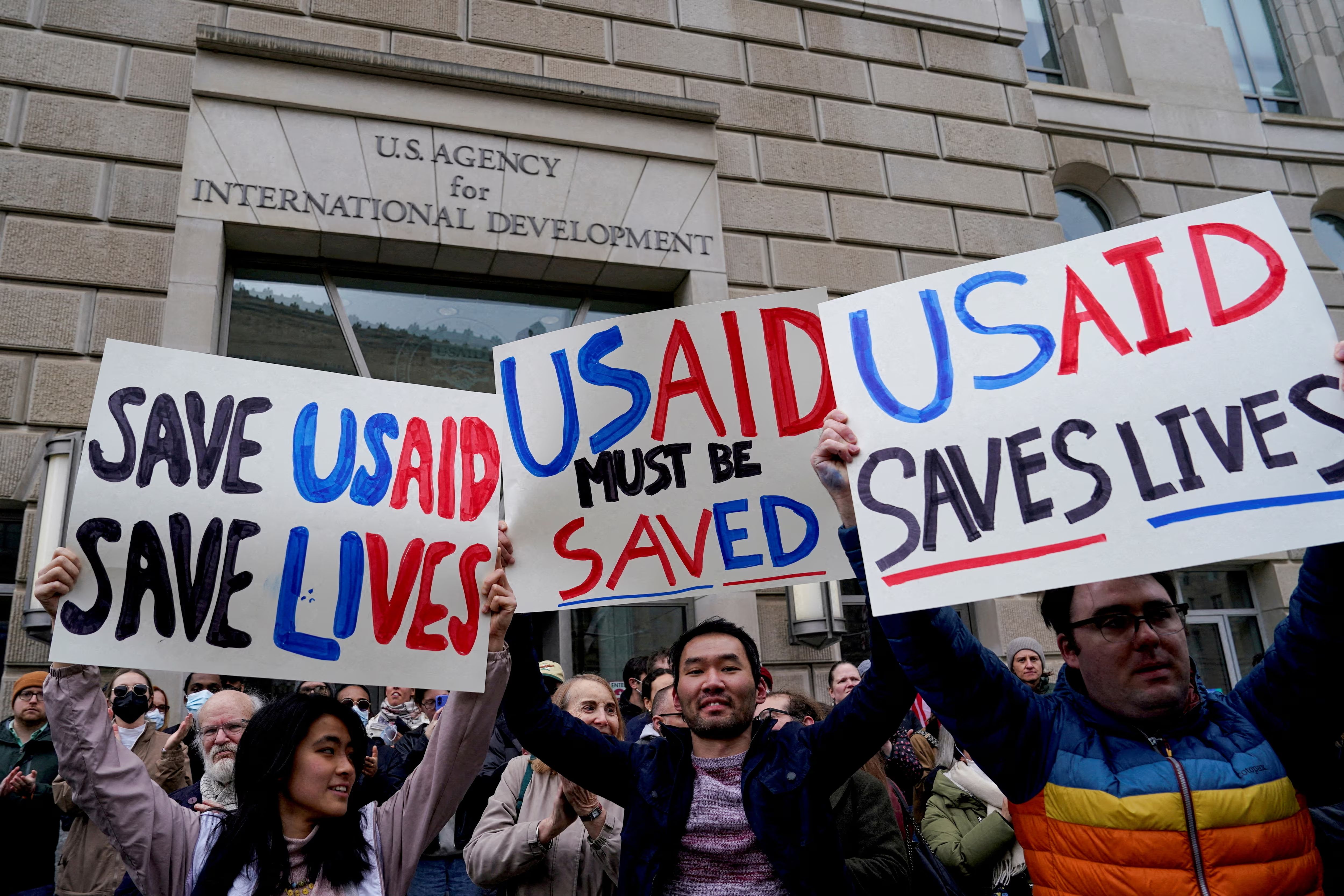 People hold placards, as the USAID building sits closed to employees after a memo was issued advising agency personnel to work remotely, in Washington, DC, February 3, 2025.