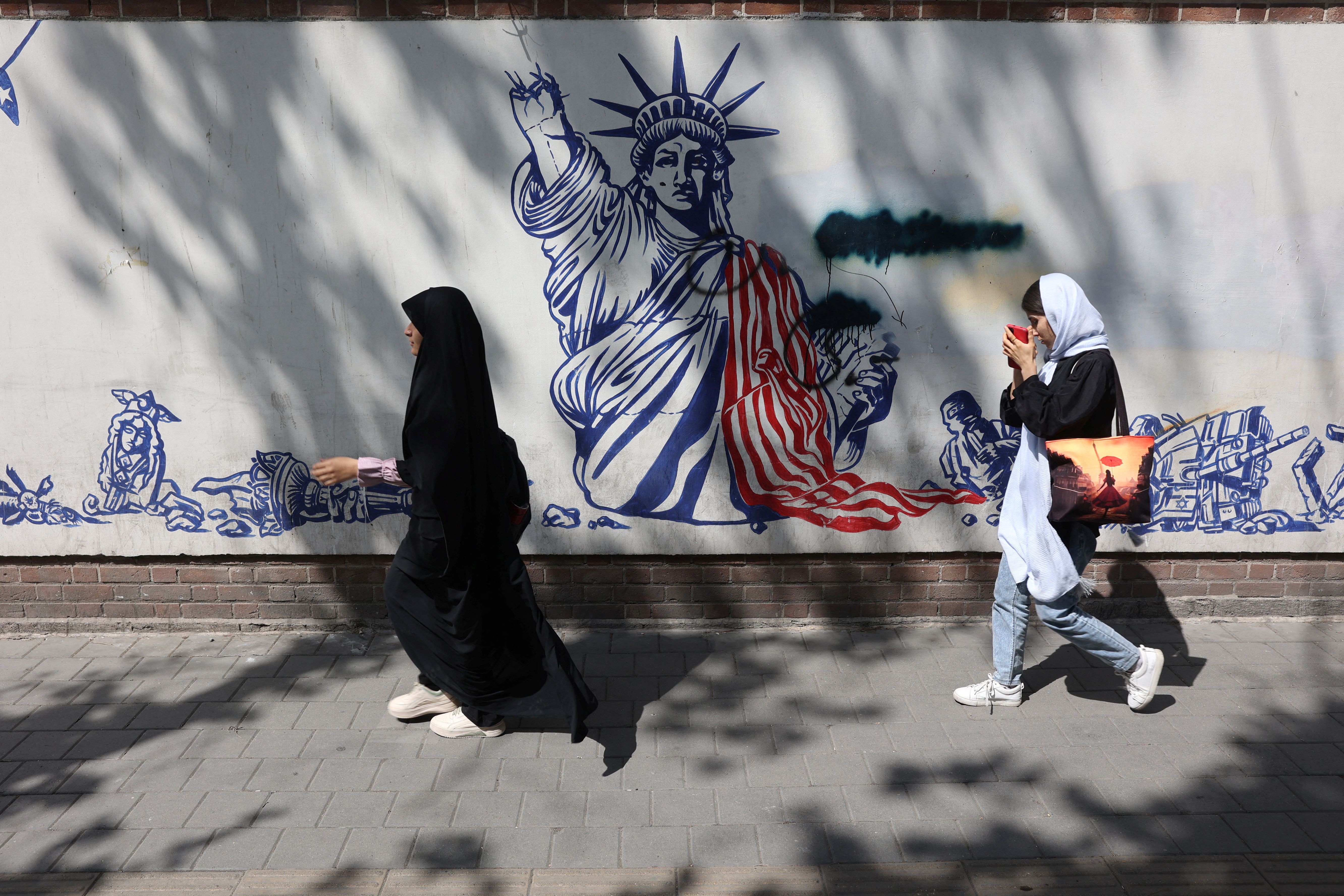 Women walk in front of new anti-US murals on the walls of the former US embassy in Tehran, Iran