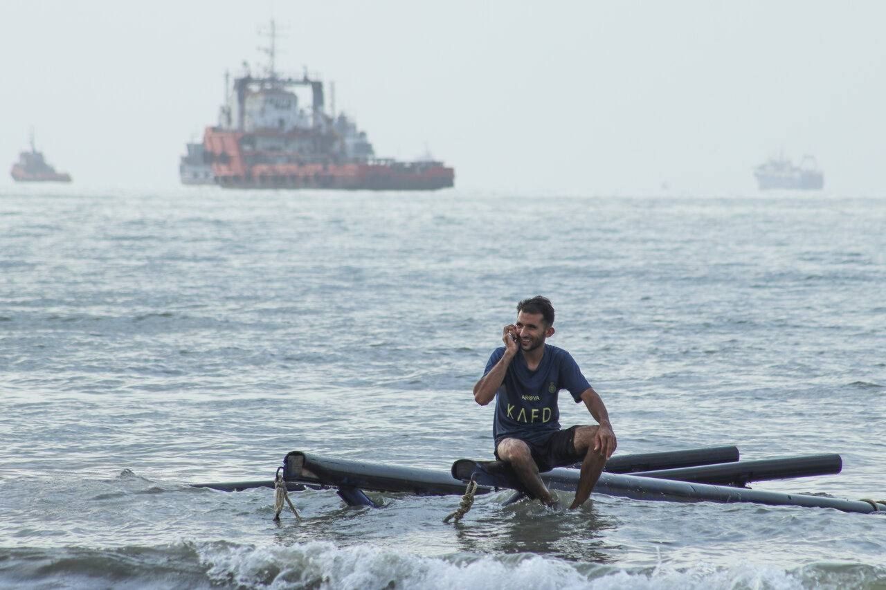 A man speaks on a mobile phone while sitting on floating pipes in the Strait of Hormuz on on July 27, 2026.