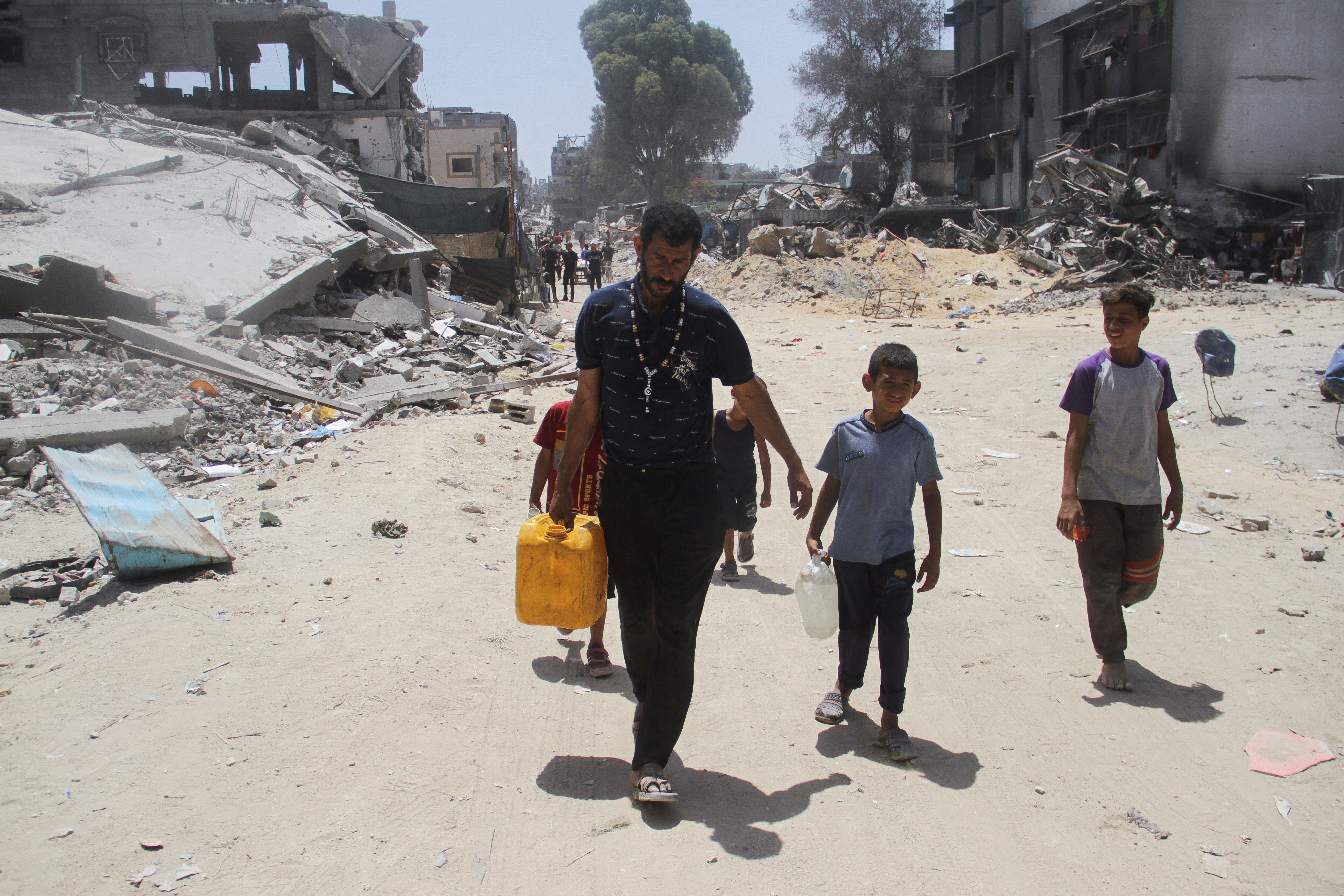 آوارگان فلسطینی در حال حمل ظروف آب در میان ویرانه‌های اردوگاه جبالیا، شمال نوار غزه، ۱۹ خرداد