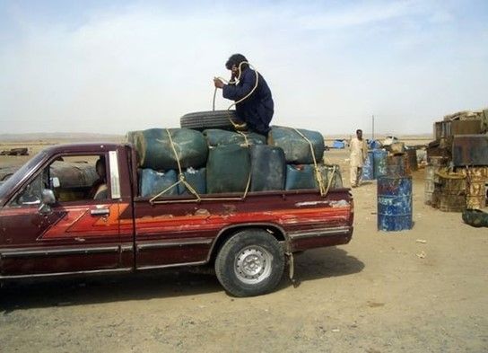 A man sits on top of plastic canisters of fuel as he prepares to unload them from a van at a roadside shop near a Pakistan and Iran border February 2013