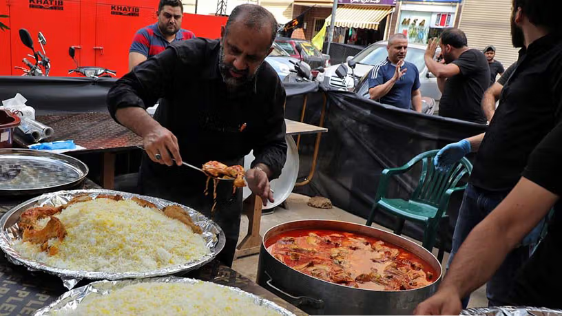 A man serves hot rice and stew to pilgrims during Arbaeen, offering free votive food.