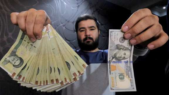 A money changer poses for the camera with a US hundred dollar bill (R) and the amount being given when converting it into Iranian rials (L), at a currency exchange shop in Tehran's business district, Iran, January 20, 2016.