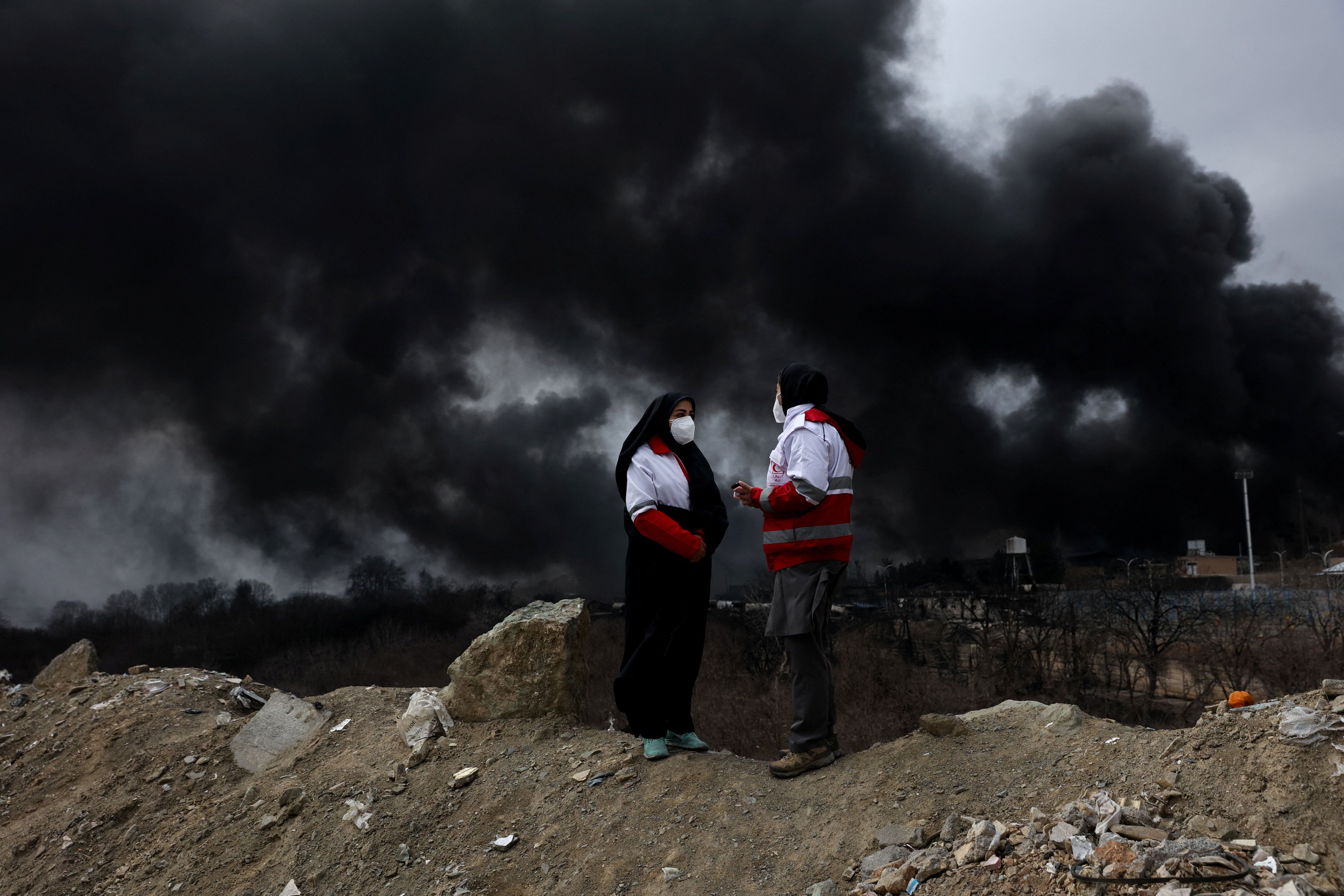 Members of the Red Crescent talk to each other as smoke rises after a reported strike on Shahran fuel tanks, amid the US-Israeli conflict with Iran, in Tehran, Iran, March 8, 2026. 