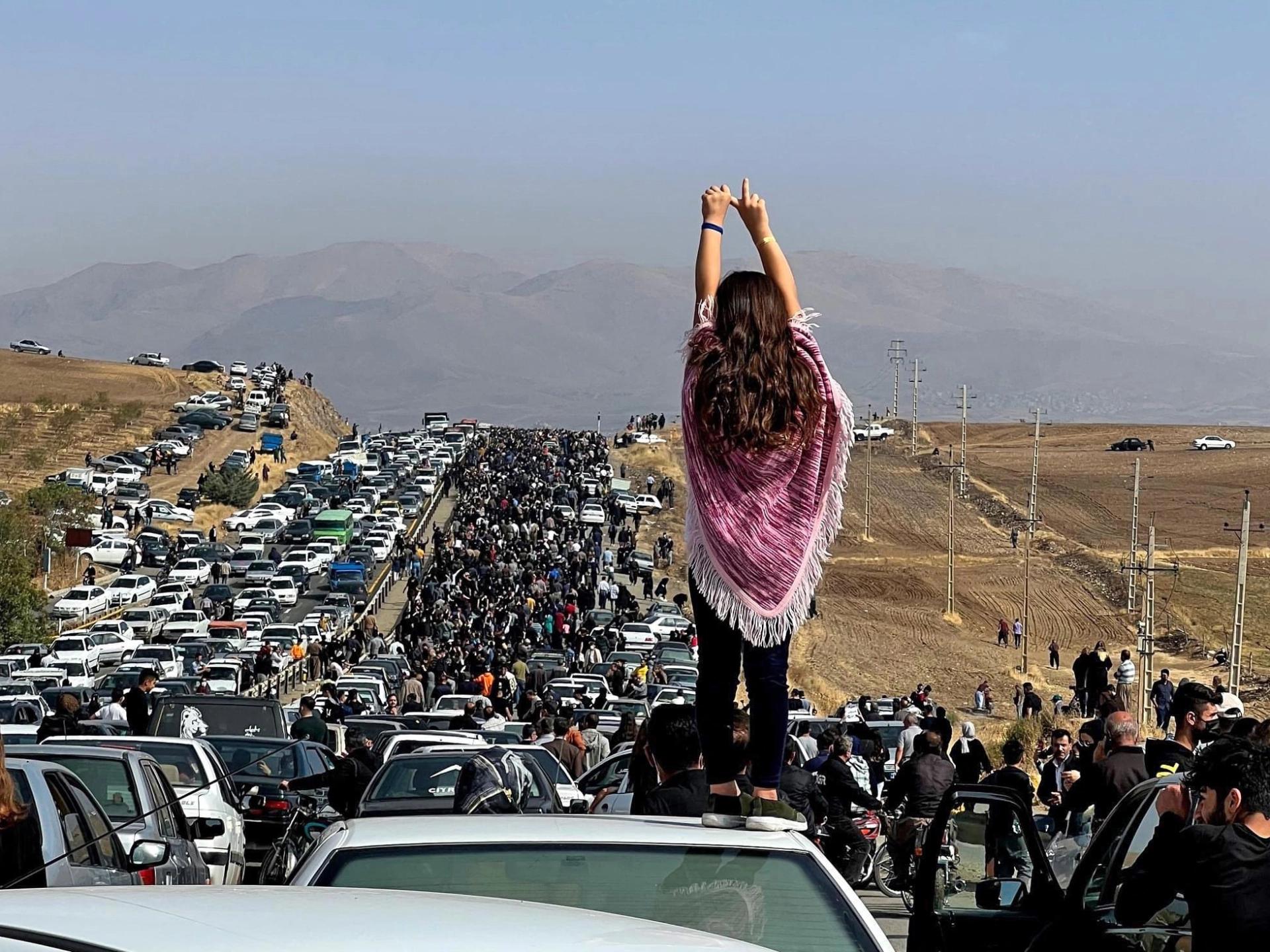 A woman stands on top of a car as protesters make their way toward the cemetery where Mahsa Amini is buried.