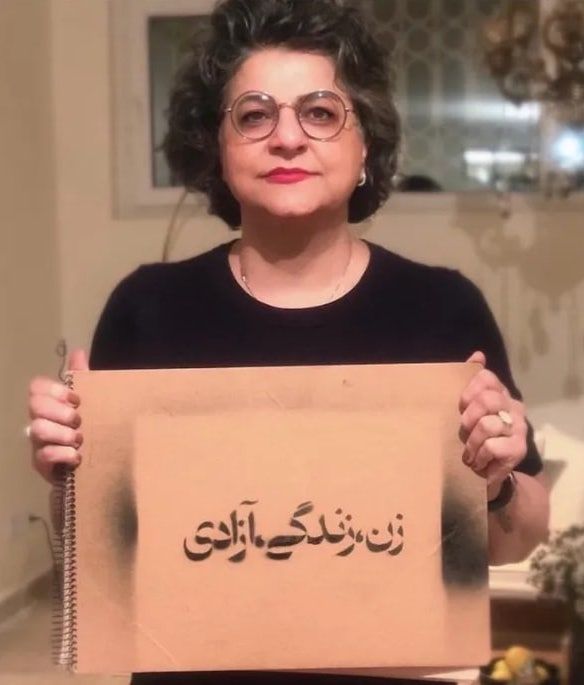 Mina Akbari holding a sign that reads, "Woman, Life, Freedom"—a slogan that emerged from the protests in Iran following the death of Mahsa Amini in September 2022