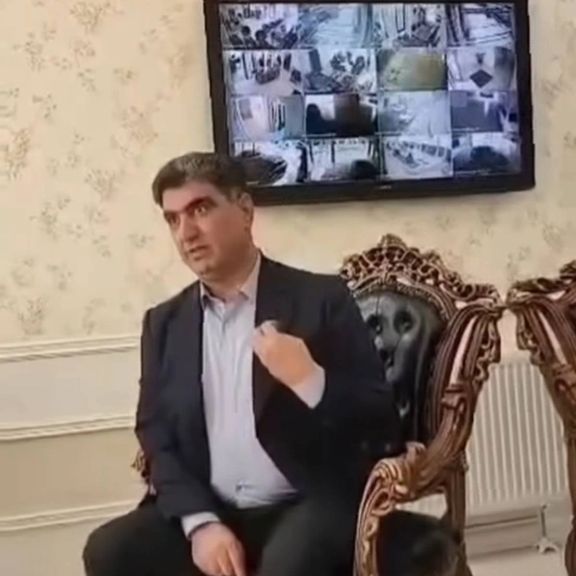 تصویری از خسرو علیکردی در مقابل تصاویر دوربینهای دفتر کارش