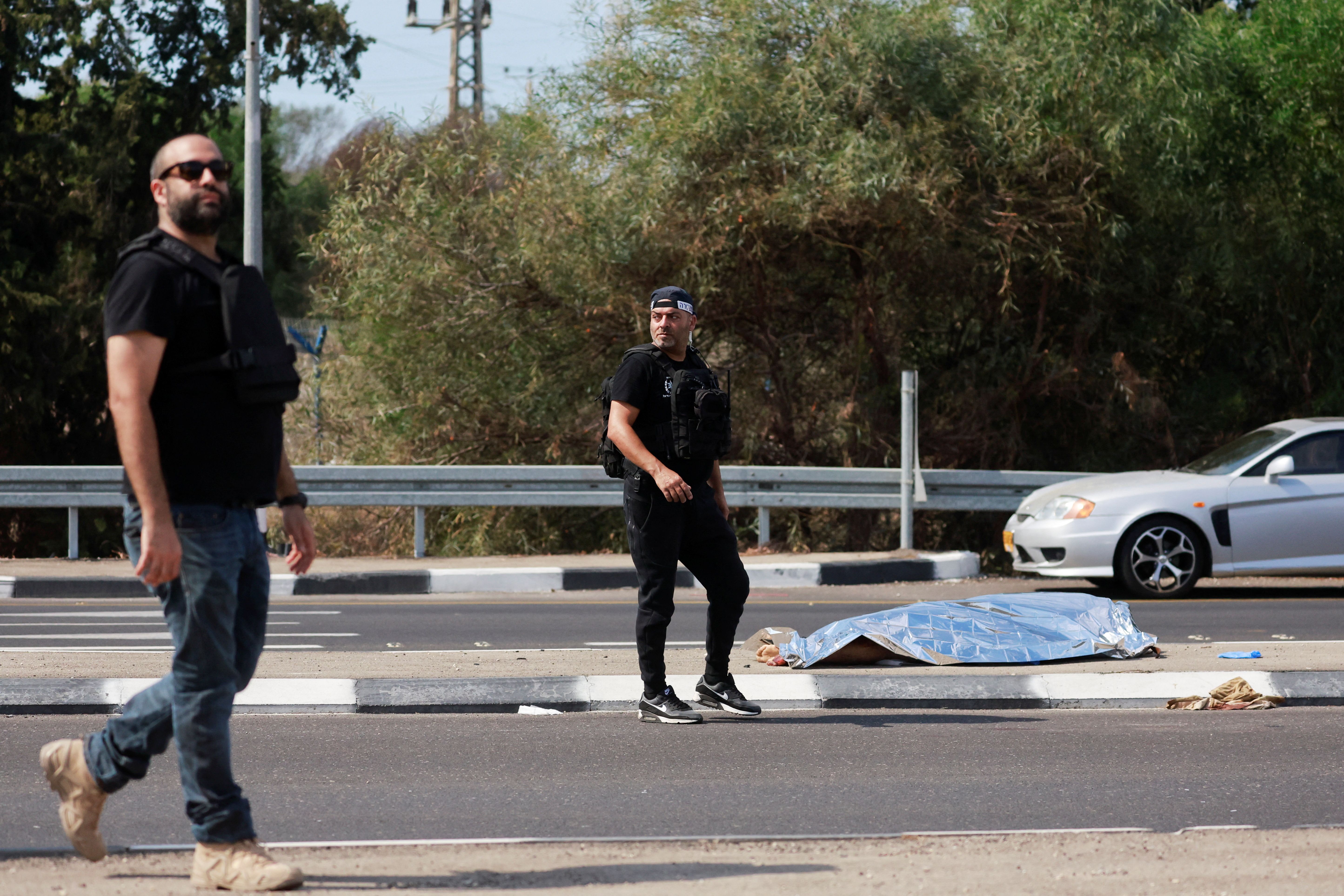 Israeli security personnel walk near the body of a dead man near Ashkelon, southern Israel October 7, 2023.