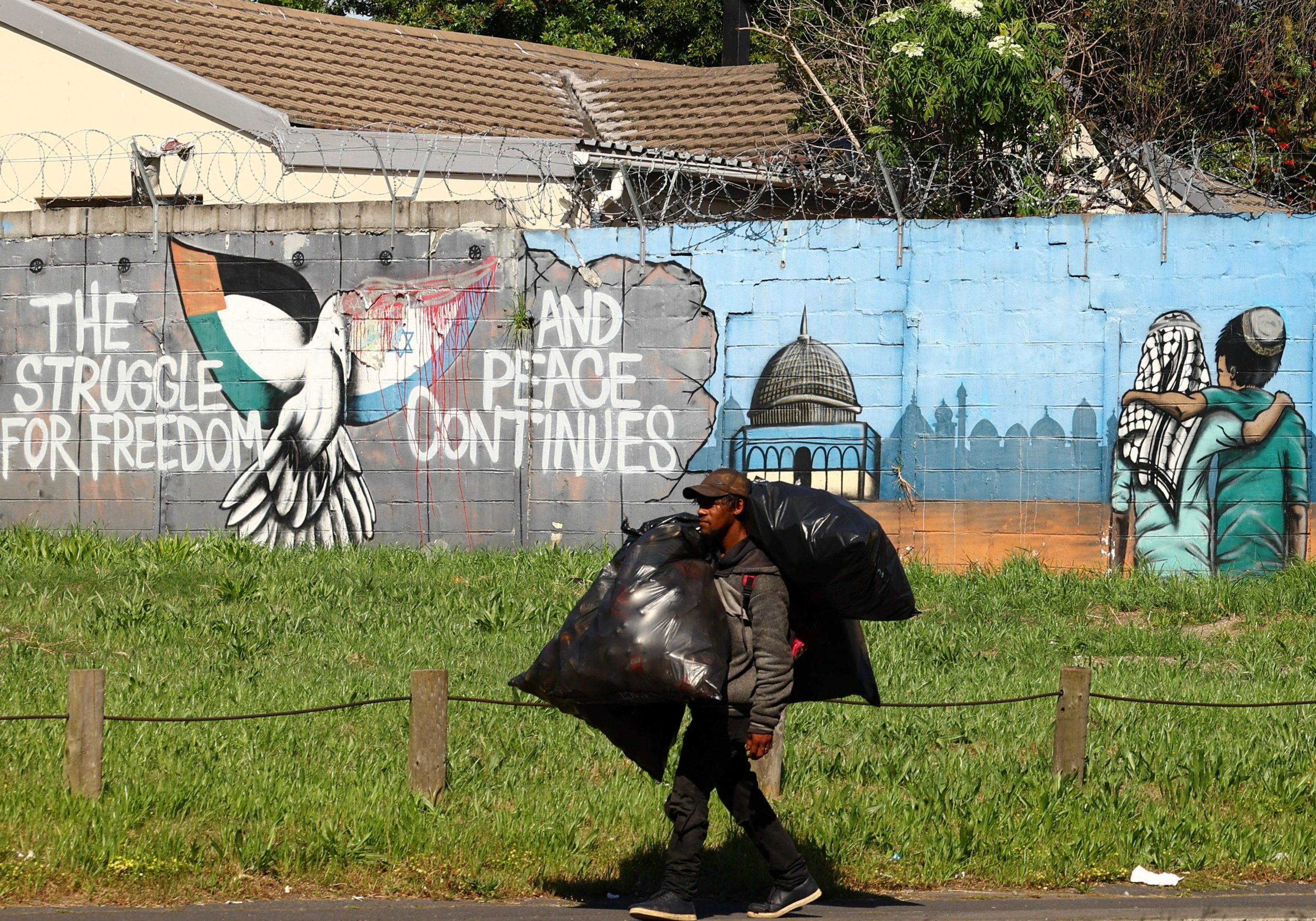 A man carries bags as he walks past a mural symbolising freedom and peace between Israel and Palestinians, in Rondebosch, Cape Town, South Africa, October 11, 2023.