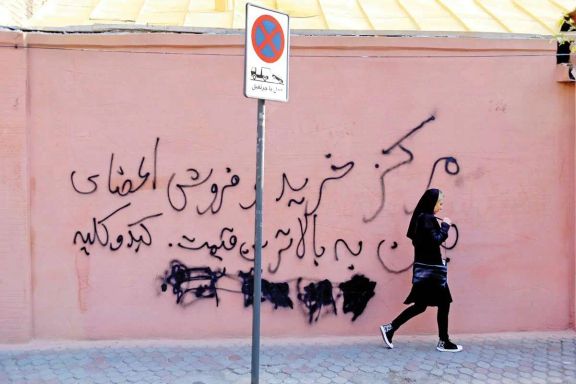 An Iranian woman walking past a wall displaying an advertisement for the sale of body organs