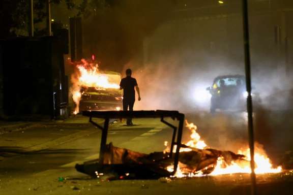 A person stands near a burning vehicle amid unrest following the death of a 17-year-old teenager killed by a French police officer during a traffic stop, France, July 1, 2023.