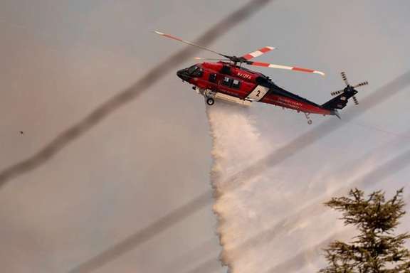 A helicopter drops water on the Palisades Fire, one of several simultaneous blazes that have ripped across Los Angeles County, along Mandeville Canyon, in the Encino neighborhood of Los Angeles, California, US, January 11, 2025.