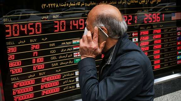File photo of an Iranian man passing in front of a board that shows exchange rates against rial