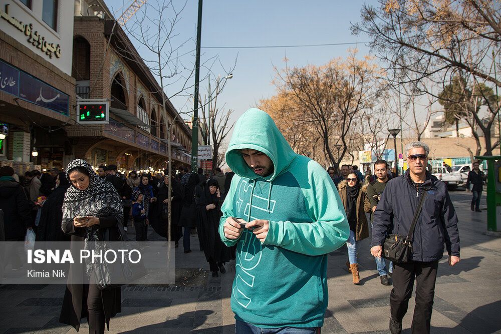 People looking at their cellphones on a street near Tehran's bazaar 