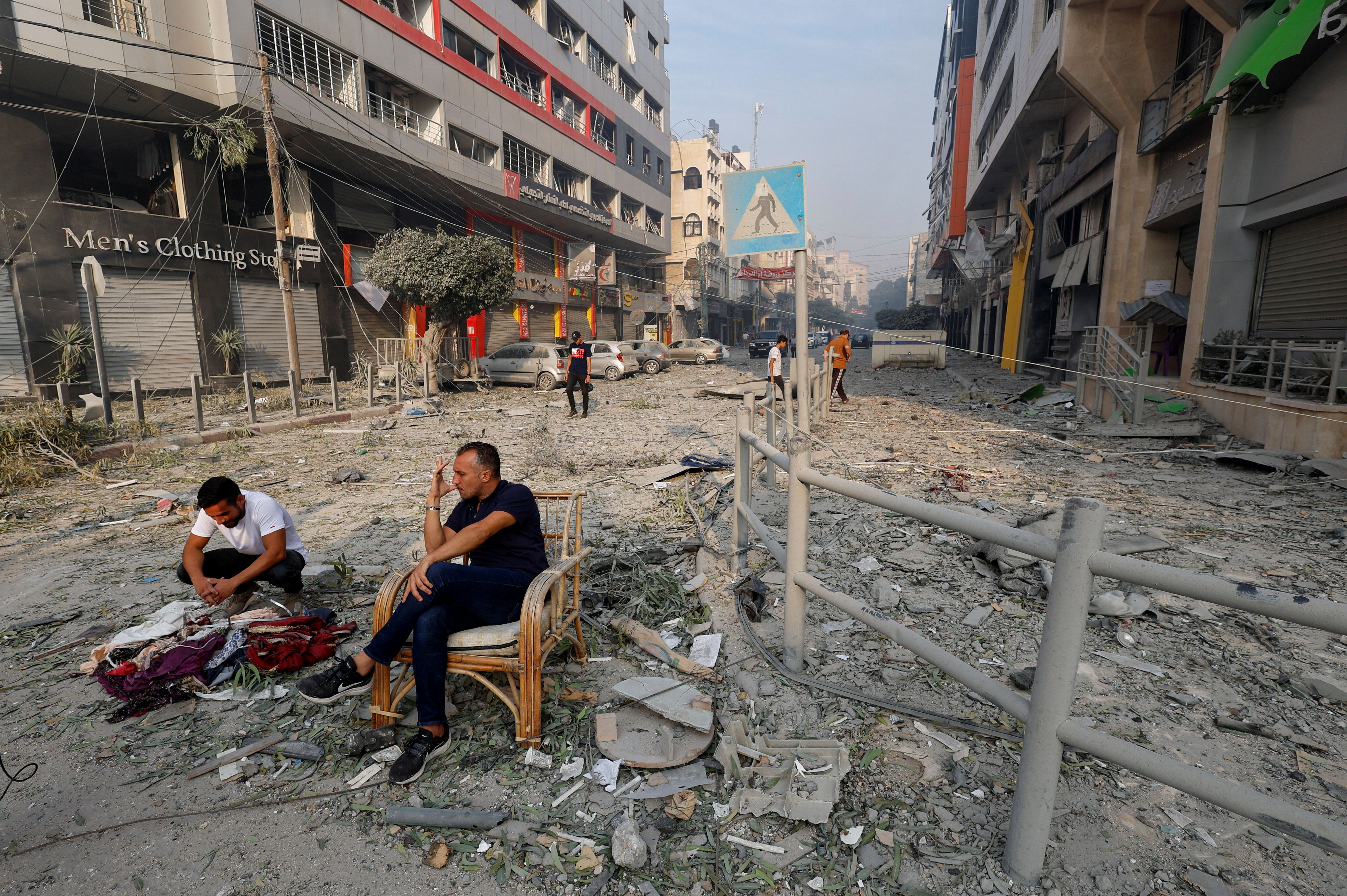 Palestinians sit on a debris-strewn street near the Watan Tower, which was destroyed in Israeli strikes, in Gaza City October 8, 2023.