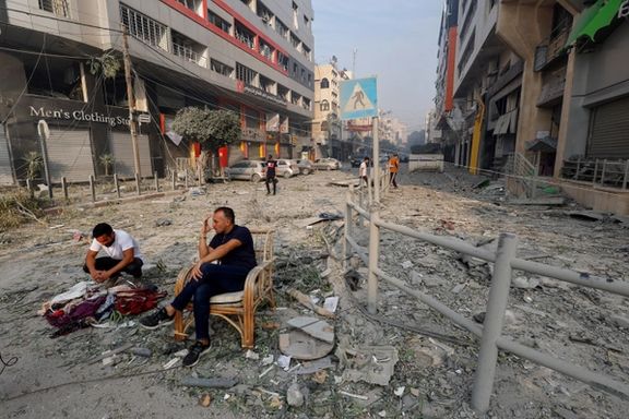 Palestinians sit on a debris-strewn street near the Watan Tower, which was destroyed in Israeli strikes, in Gaza City October 8, 2023.