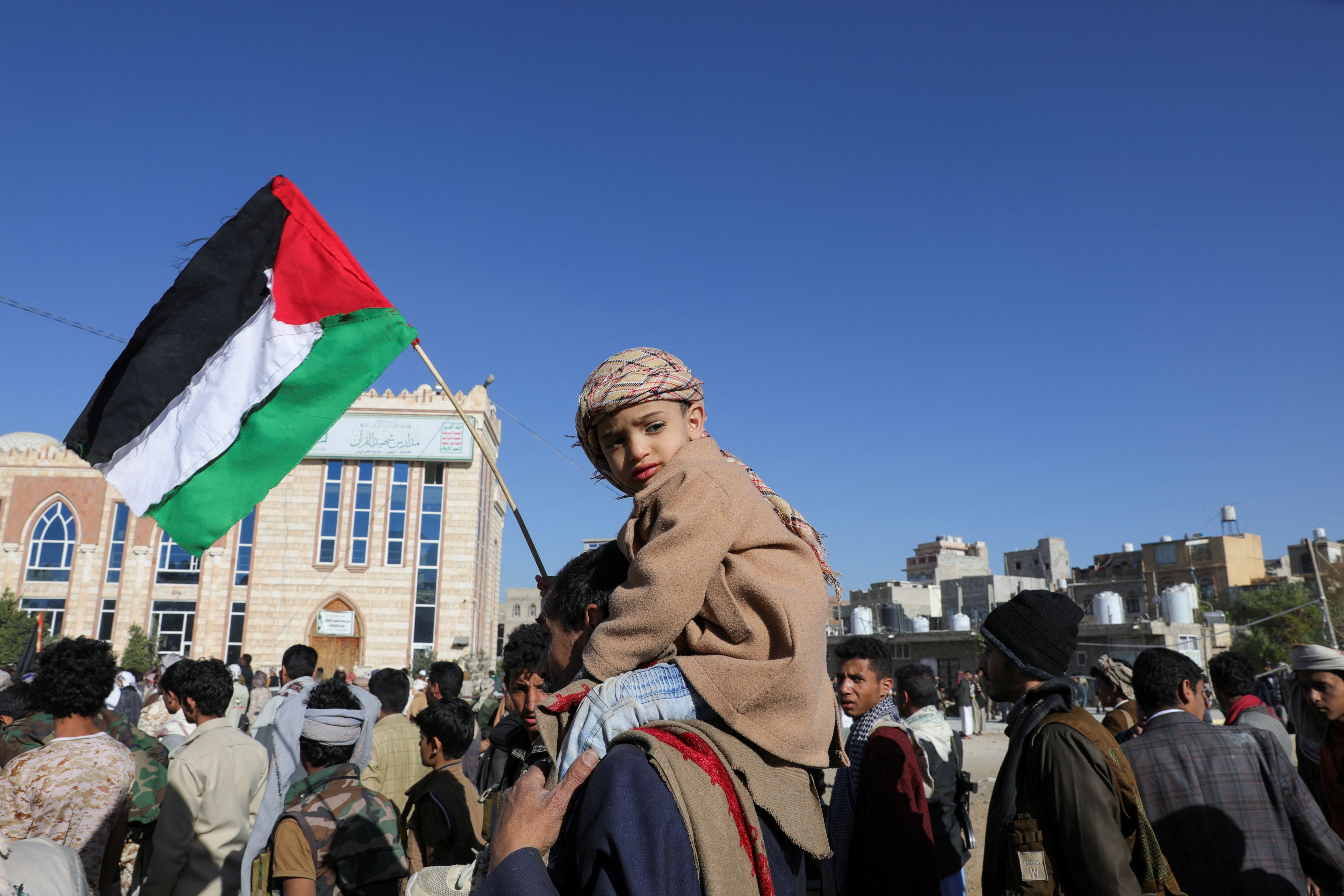 The son of a newly recruited Houthi fighter holds the Palestinian flag as his father carries him during a ceremony at the end of the training of new recruits in Sanaa, Yemen January 11, 2024. 