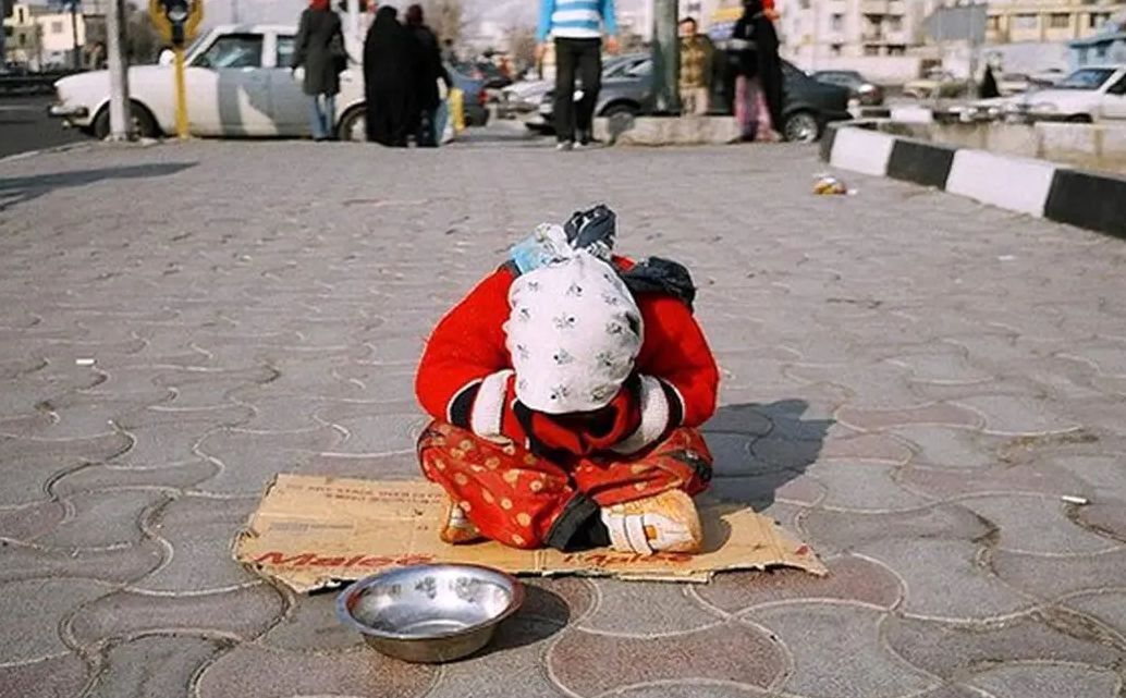 A little girl sitting on the sidewalk asking for change, Iran