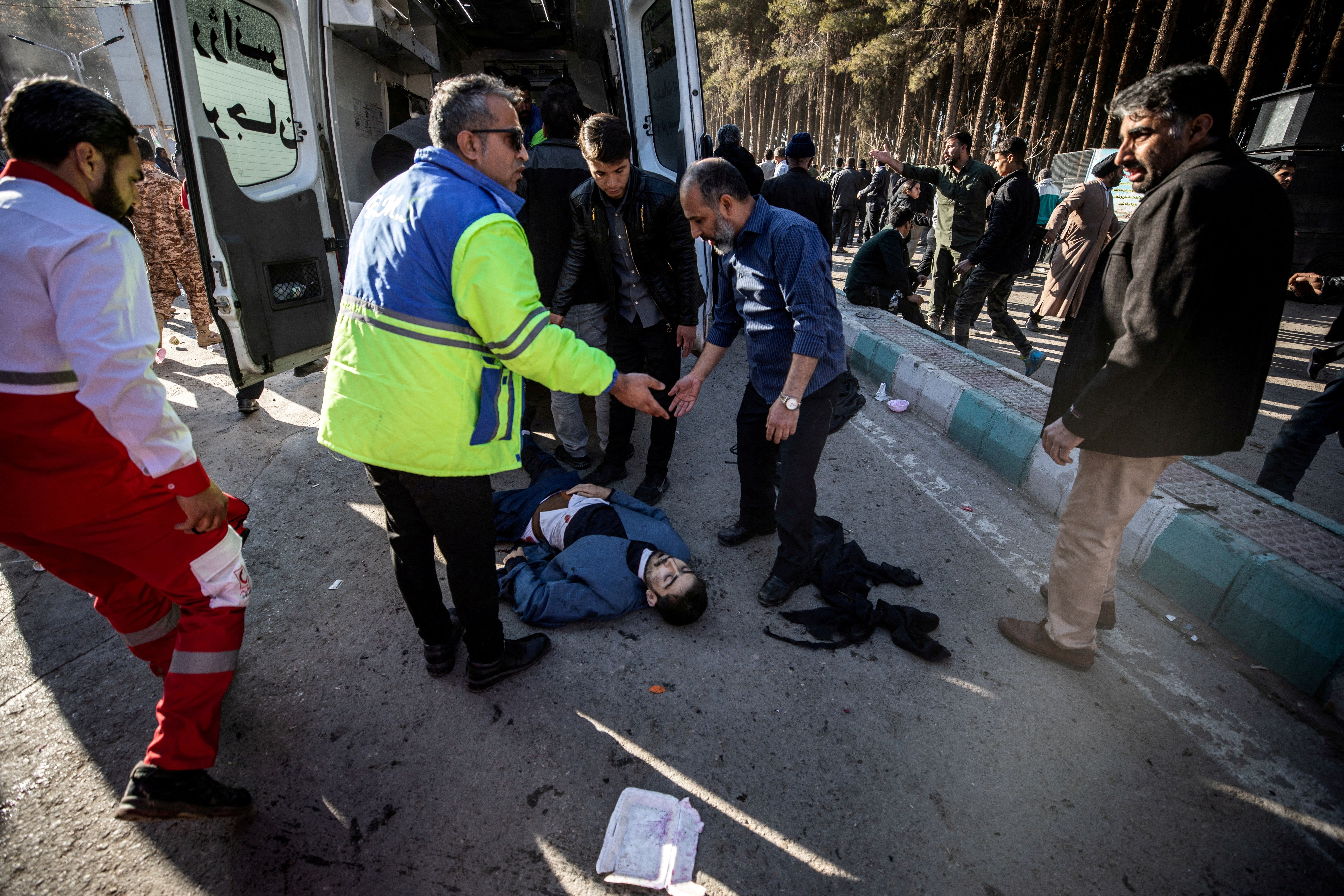 People stand near a man lying on the ground at the scene of explosions in Kerman, January 3, 2024.