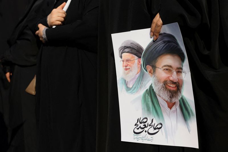 A woman holds a portrait of Mojtaba Khamenei, with his father Ali Khamenei pictured in the background.