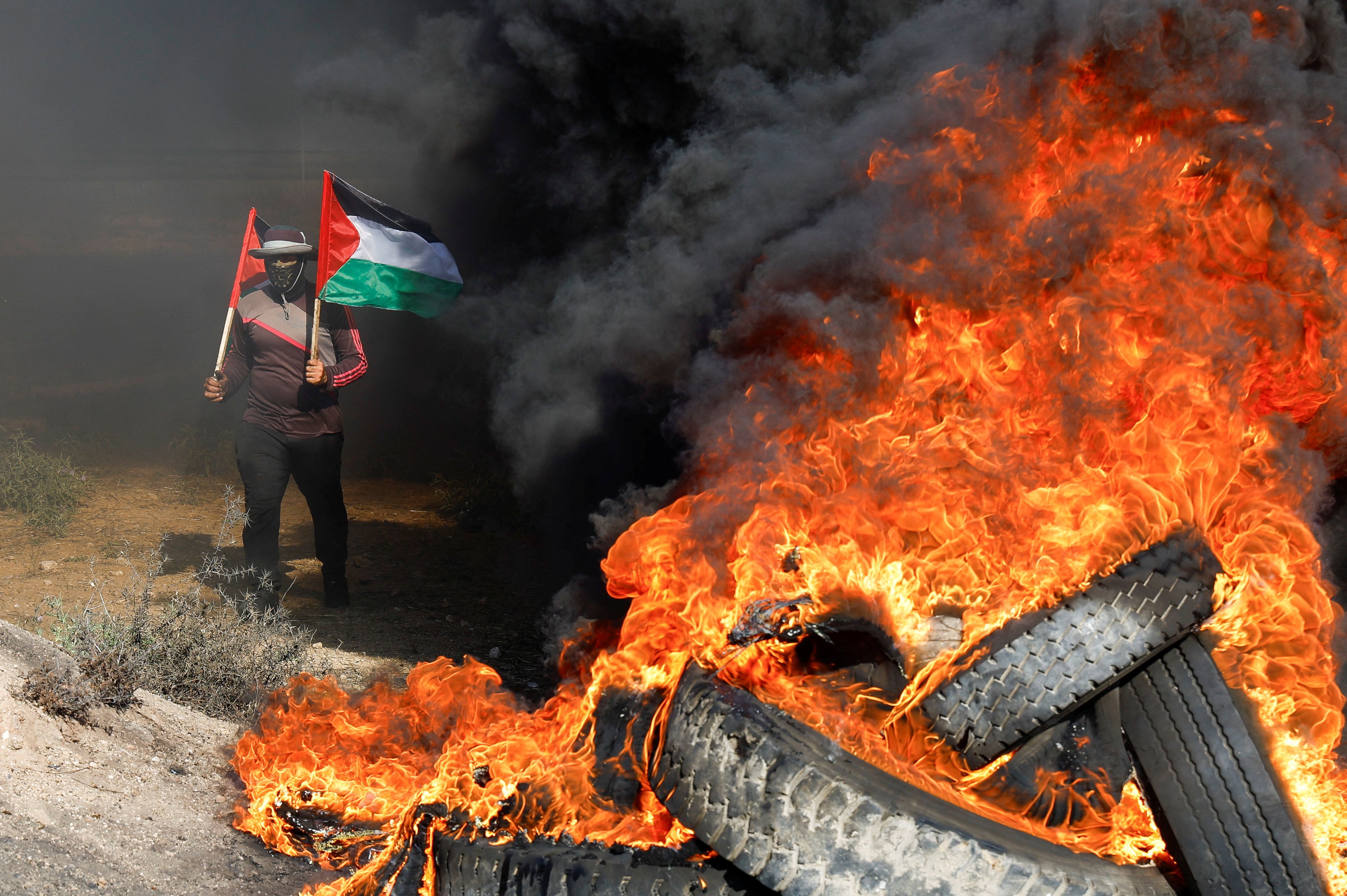 A Palestinian holds flags during a protest against Israeli army raid in Jenin, along Israel-Gaza border fence east of Gaza City July 3, 2023.