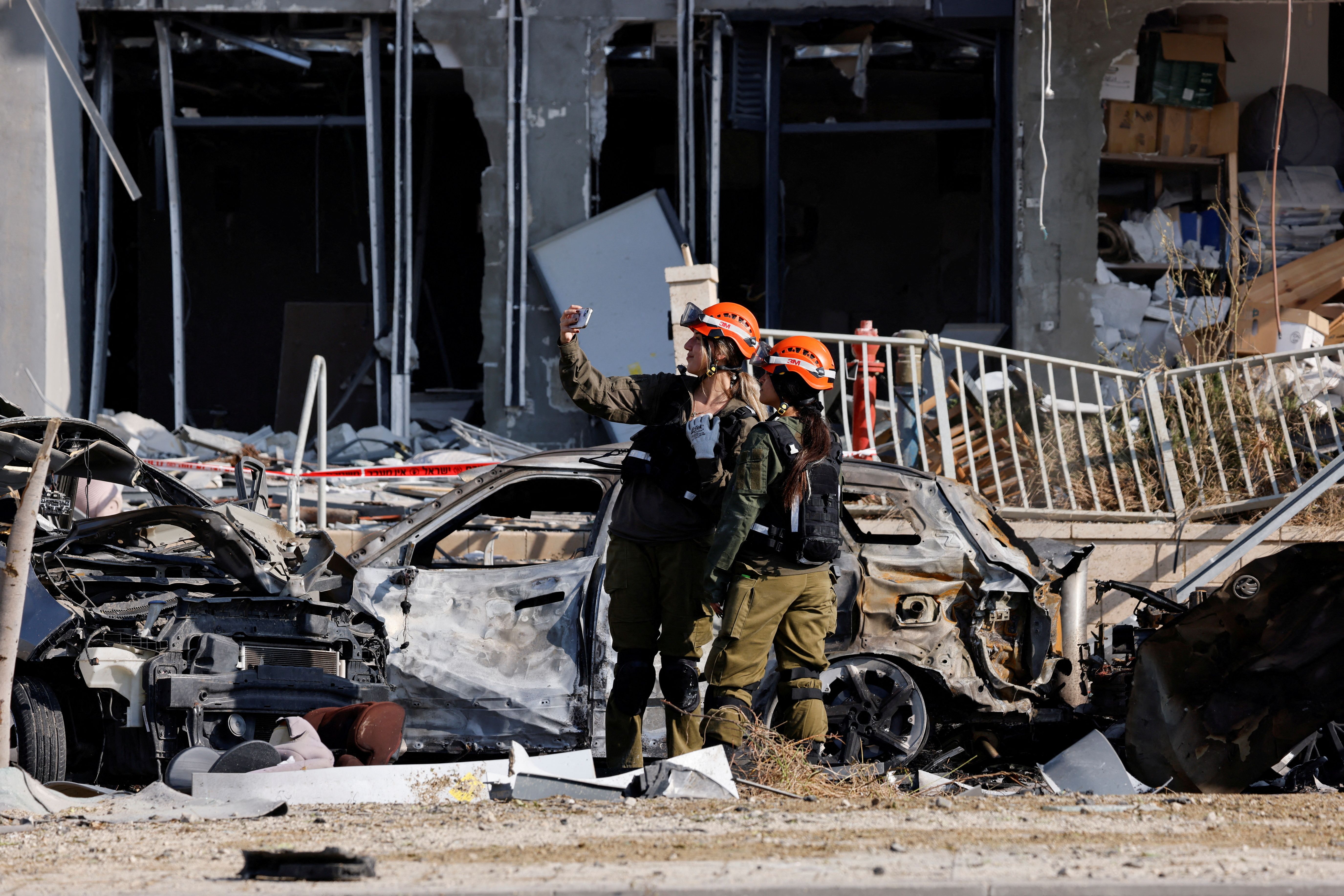 Israeli soldiers take selfies next to destroyed cars and a damaged residential building at an impact site following Iran's missile strike on Israel, in Be'er Sheva, Israel, June 20, 2025. 