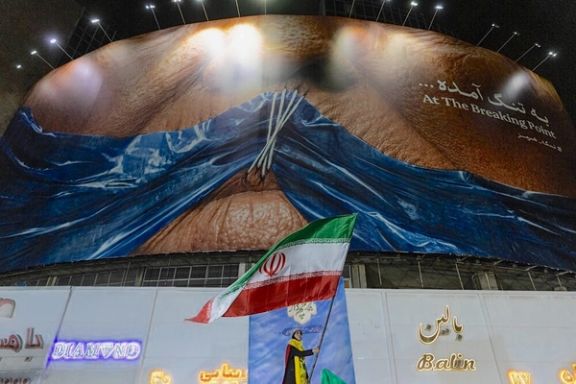 A woman waves an Iranian flag beneath a giant anti-US billboard depicting, in a state-backed rally in Tehran, May 9, 2026